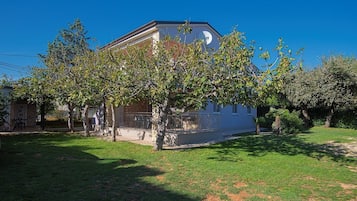Une maison à deux étages dotée d’un balcon, entourée d’une pelouse bien entretenue et d’arbres.