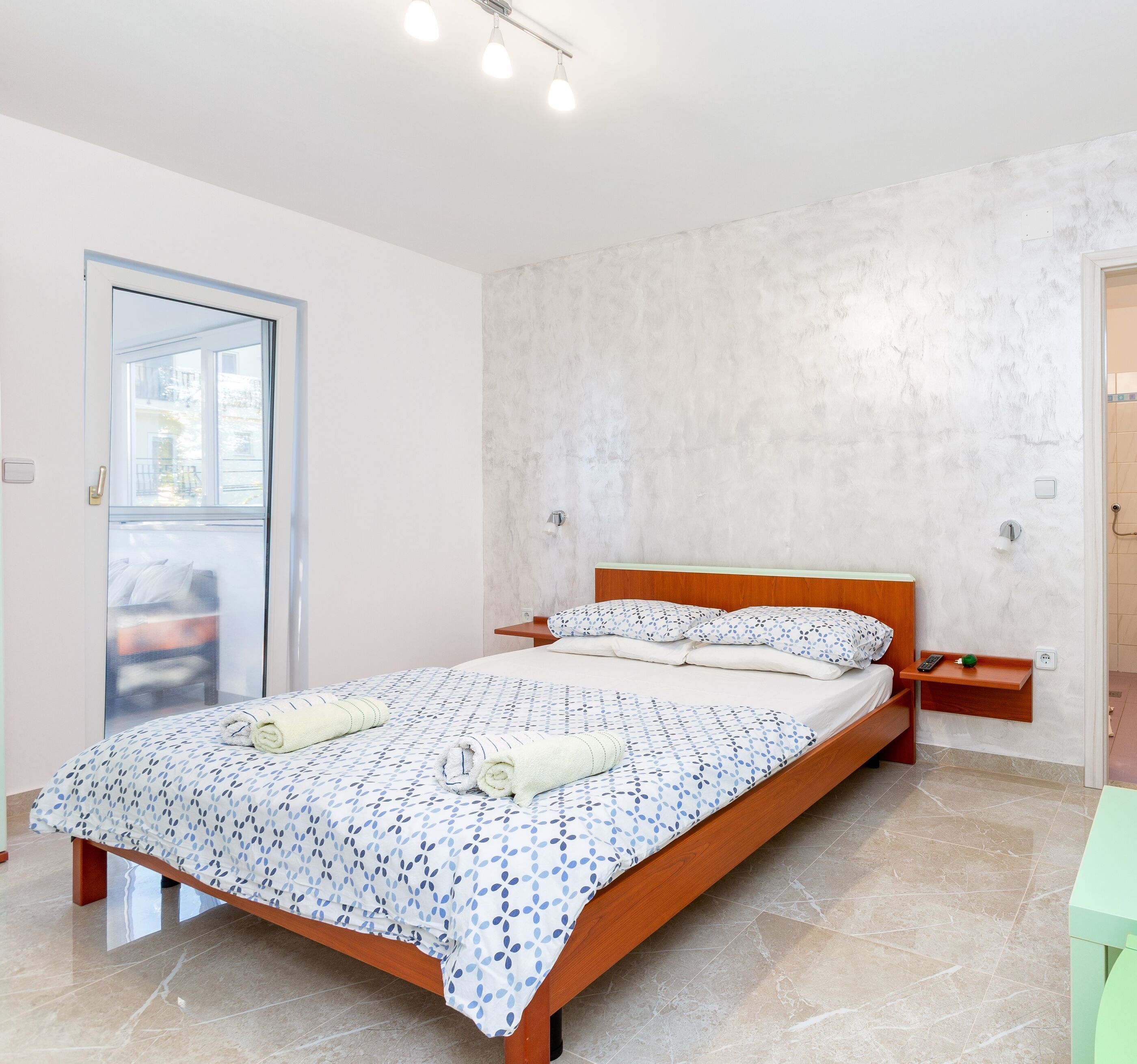 Een moderne slaapkamer met een groot bed, een houten hoofdbord, een nachtkastje en uitzicht door een glazen deur.