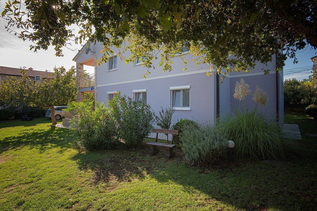A two-story house with a balcony, surrounded by a well-maintained garden with a bench and various plants.