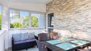 Un balcon avec un canapé en osier, une table en bois avec des chaises et un mur en pierre.