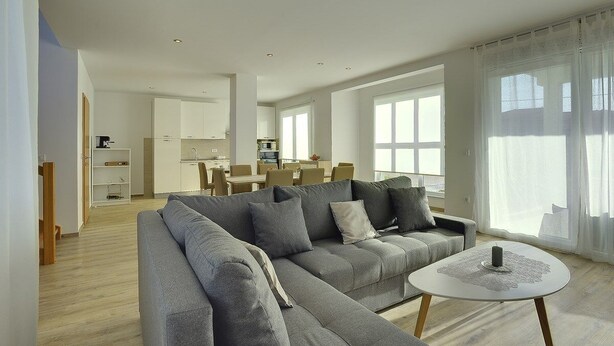 A modern living room with a grey sectional sofa, a round coffee table, and a dining area in the background.