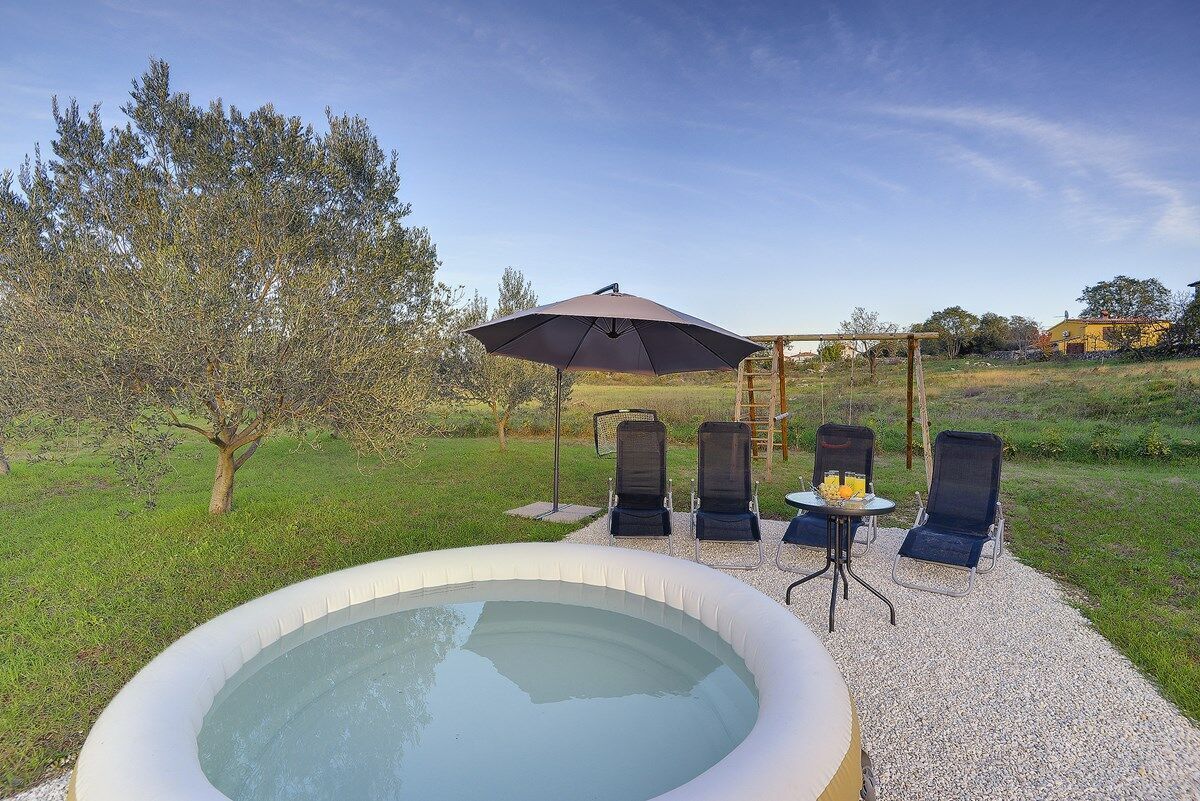 An outdoor hot tub area with a pergola, lounge chairs, and a table with drinks.