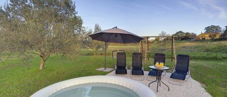 An outdoor hot tub area with a pergola, lounge chairs, and a table with drinks.