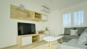 A modern living room with a flat-screen TV, wooden shelves, a small table, and a grey sofa.