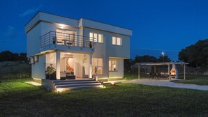 A modern two-story house with a balcony, a patio with outdoor seating, and a wood-burning stove.