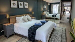 Een moderne slaapkamer met een groot bed, nachtkastjes, een spiegel en lijstwerken aan de muur.