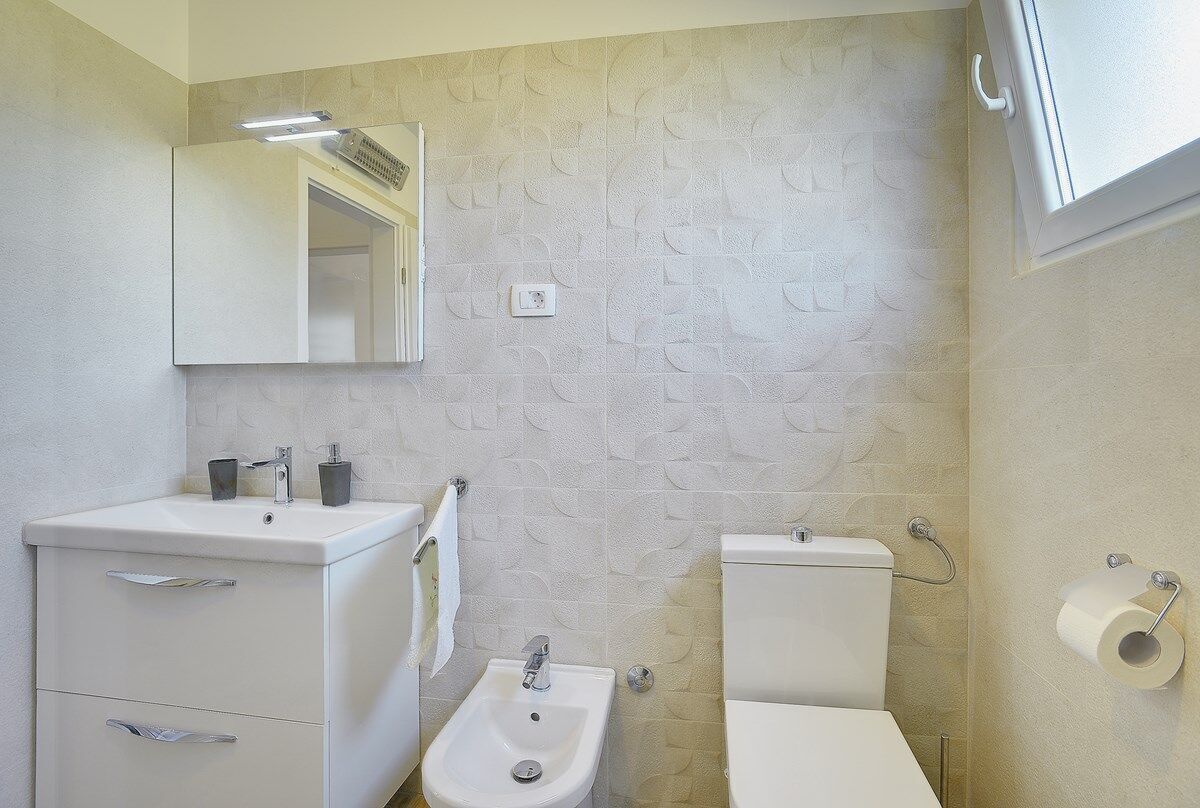 A bathroom with a white sink, bidet, toilet, and a mirror above the sink.