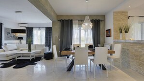 Un soggiorno moderno con zona pranzo, caratterizzato da un lampadario, arredi bianchi e una parete decorata in pietra.