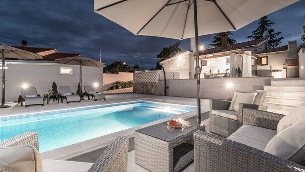 Une piscine entourée de chaises longues et d’une table, avec des parasols et un espace de repos abrité.