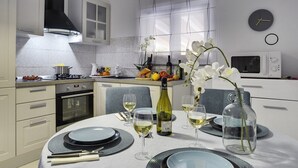 Une cuisine moderne avec des meubles blancs, une hotte noire et un coin repas agrémenté d’assiettes, de verres et d’une bouteille de vin.