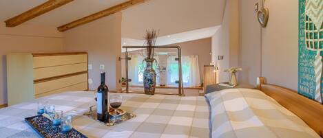 A bedroom with a checkered bedspread, a bedside table with a vase and a bottle, and a window with curtains.