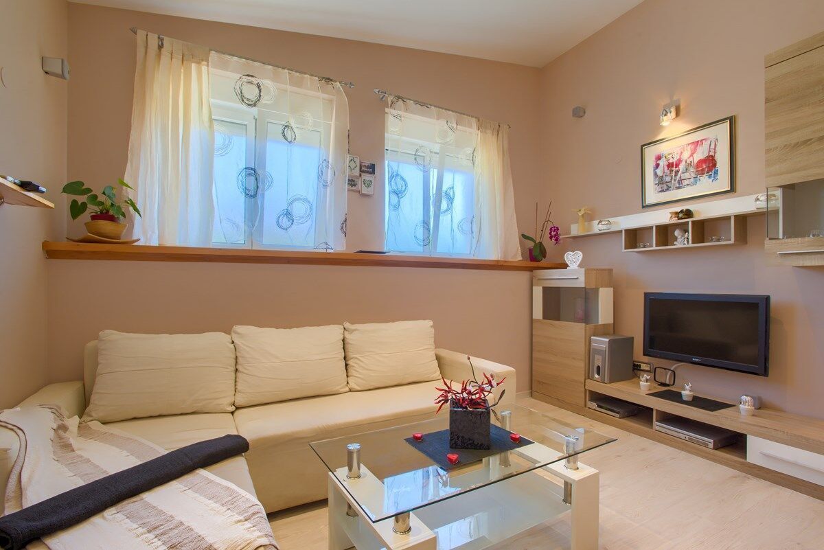 Una sala de estar moderna con un sofá, una mesa de centro de vidrio, un televisor y una ventana con cortinas.