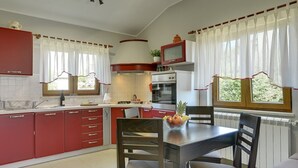 A kitchen with red cabinets, a dining table with chairs, a microwave, and a window with curtains. - Villa Maria Betiga (73946-K1) - Fazana (Fazana)