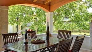 An outdoor patio with a wooden table set for dining, surrounded by chairs, and a bottle of wine. - Villa Maria Betiga (73946-K1) - Fazana (Fazana)