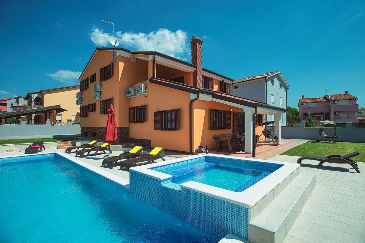 A two-story house with a swimming pool, outdoor seating, and a clear blue sky.
