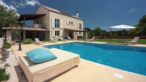 Une maison à deux étages avec une piscine, du mobilier d’extérieur et un ciel d’un bleu éclatant.