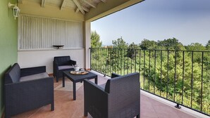 A balcony with wicker furniture, a table with a teapot, and a view of greenery.