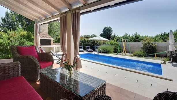 An outdoor patio with wicker furniture, a glass table, and a swimming pool.