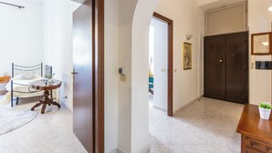 Un corridoio con un letto, un tavolo rotondo in legno e una porta di legno scuro.
