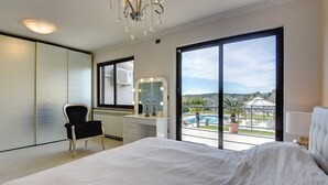 Una camera da letto con un letto grande, una toeletta con specchio, una sedia e vista su una piscina.