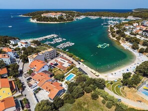 Luftaufnahme einer Küstenstadt mit einem Yachthafen, Strand und Wohnhäusern.