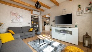 Uma sala de estar moderna com sofá cinzento, almofadas amarelas, mesa de centro de madeira, televisão de tela plana e um armário branco.