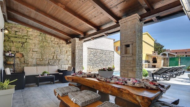 An outdoor seating area with stone walls, wooden beams, and a pool in the background. - Villa Micol (74066-K1) - Vodnjan (Vodnjan)