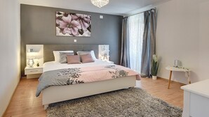 A modern bedroom with a large bed, a chandelier, a floral wall art piece, and a view of the outdoors through a window with curtains. - Villa Micol (74066-K1) - Vodnjan (Vodnjan)