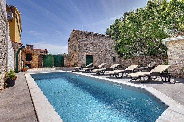 Une piscine rectangulaire, dotée de chaises longues et bordée d’un bâtiment en pierre.