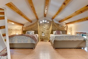 Une chambre avec deux lits, des poutres en bois, des murs en pierre et une petite table.