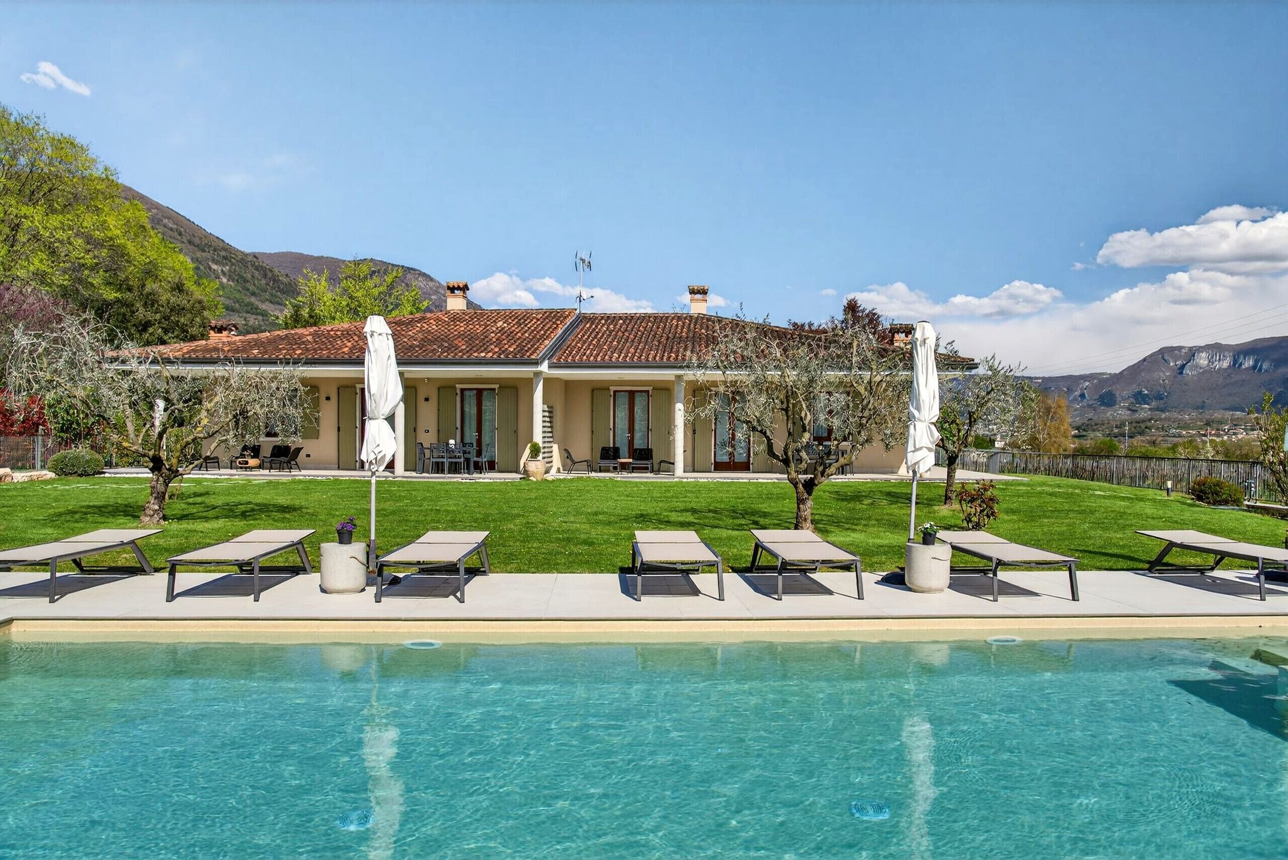 Ein Pool mit Liegestühlen, ein Haus mit Ziegeldach und eine gebirgige Kulisse.