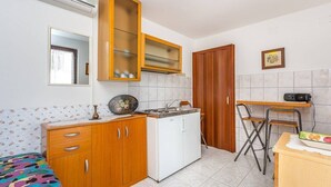 Eine kleine Küche mit Holzschränken, einem weißen Kühlschrank und einer Essecke mit einem Stuhl und einem Tisch.