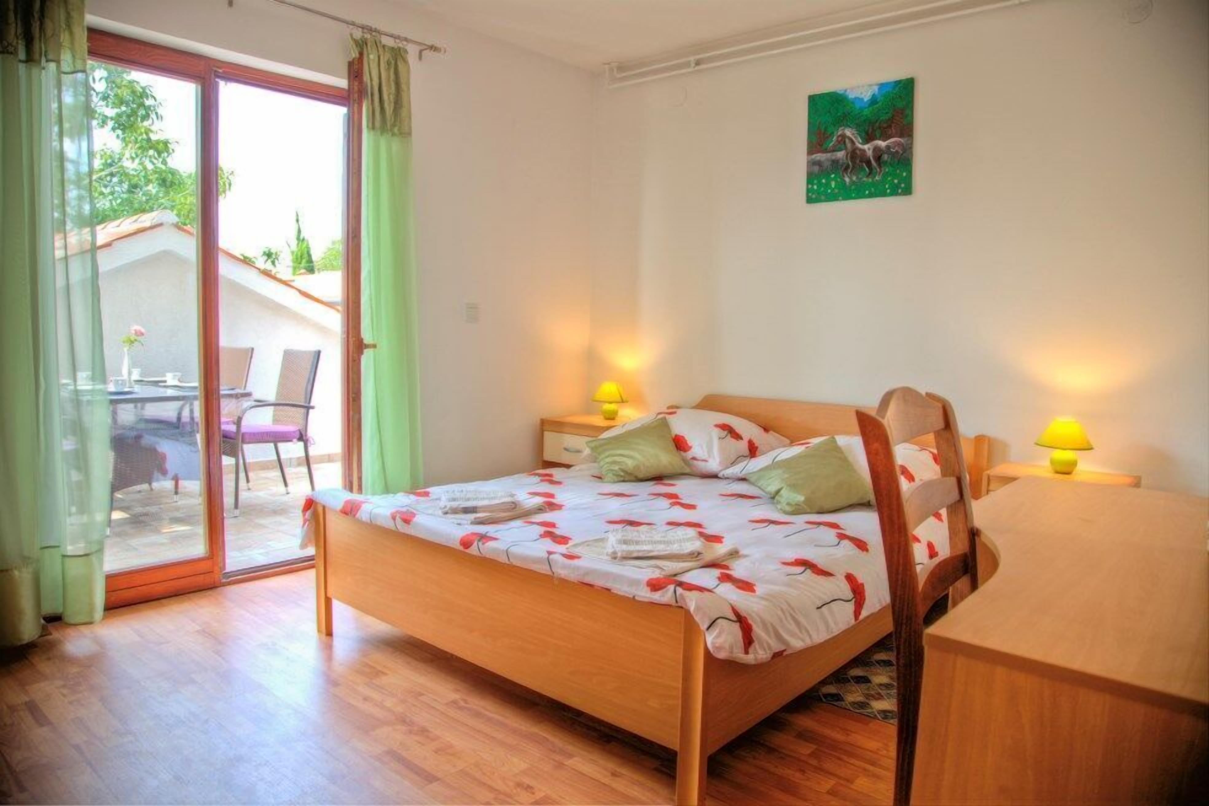 Un dormitorio con cama de madera, dos lámparas de noche, un cuadro en la pared y un ventanal corredero que da a un espacio exterior.