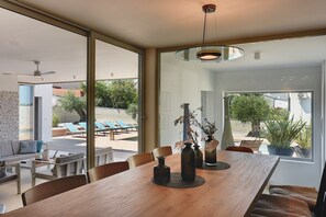 A modern dining area with a wooden table, chairs, and decorative vases. Large windows provide views of an outdoor patio with lounge chairs and greenery. - Villa Balizerka (74154-K1) - Pula (Pula)