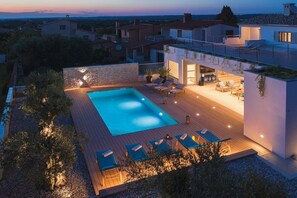 Un área de piscina moderna al aire libre con sillones de descanso y un bar, rodeada de un jardín ajardinado y vistas del barrio.