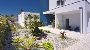A modern white building with a blue accent wall, a covered outdoor seating area, and a landscaped garden with various plants. - Villa Balizerka (74154-K1) - Pula (Pula)