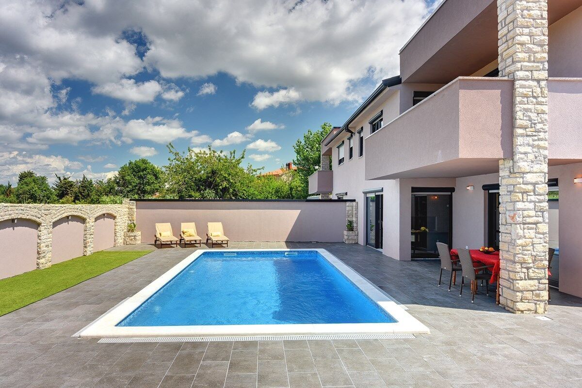 A modern pool area with a rectangular pool, stone pillars, and a dining area with outdoor seating.