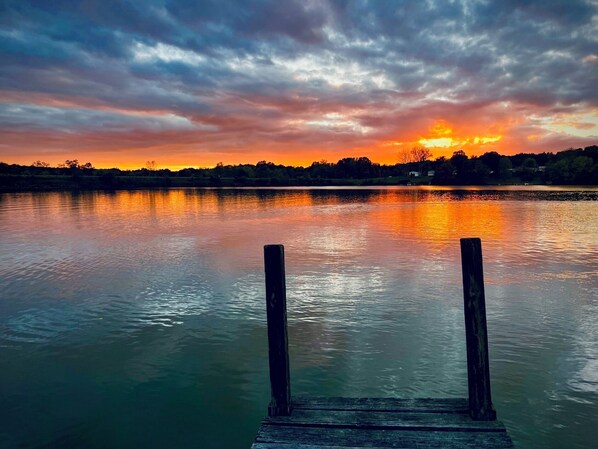 Un muelle de madera se adentra en aguas tranquilas con un atardecer al fondo.