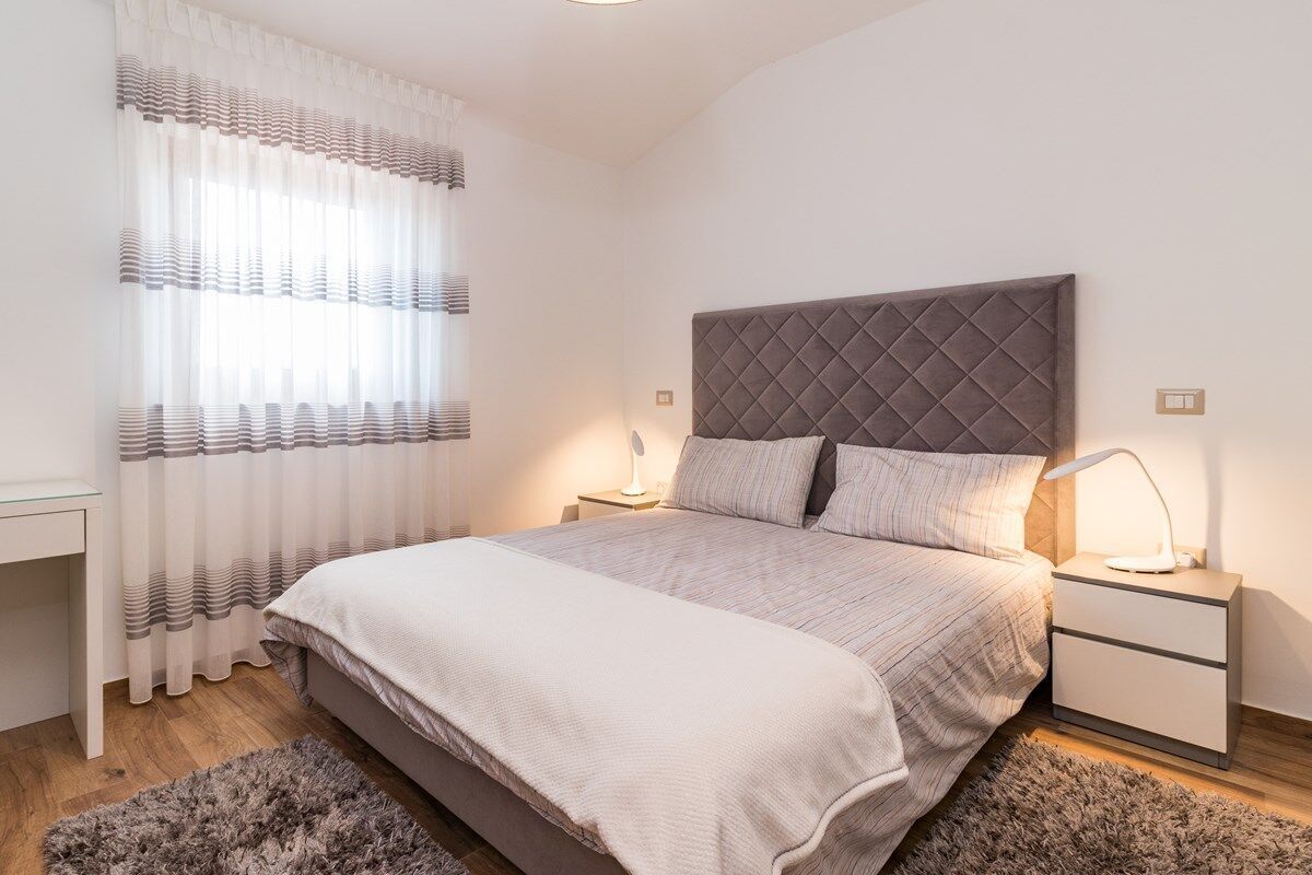 A bedroom with a bed, nightstands, a lamp, a window with curtains, and a rug.