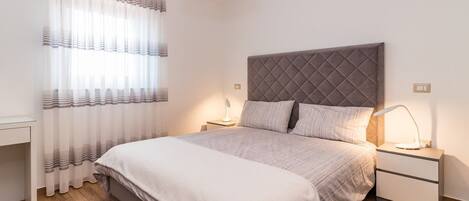 A bedroom with a bed, nightstands, a lamp, a window with curtains, and a rug.