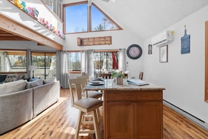 A spacious living area with a high ceiling, wooden beams, a large window, and a cozy seating arrangement. - Carebear Cabin: Cowboy Game Room & Lake Access (Blakeslee)