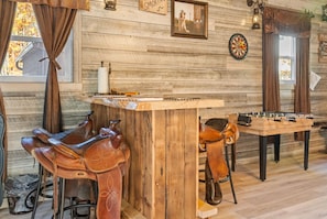 A rustic room with wooden walls, a dartboard, a foosball table, and leather chairs. - Carebear Cabin: Cowboy Game Room & Lake Access (Blakeslee)