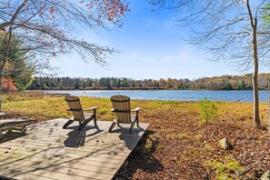 A wooden deck with two Adirondack chairs facing a lake. - Carebear Cabin: Cowboy Game Room & Lake Access (Blakeslee)