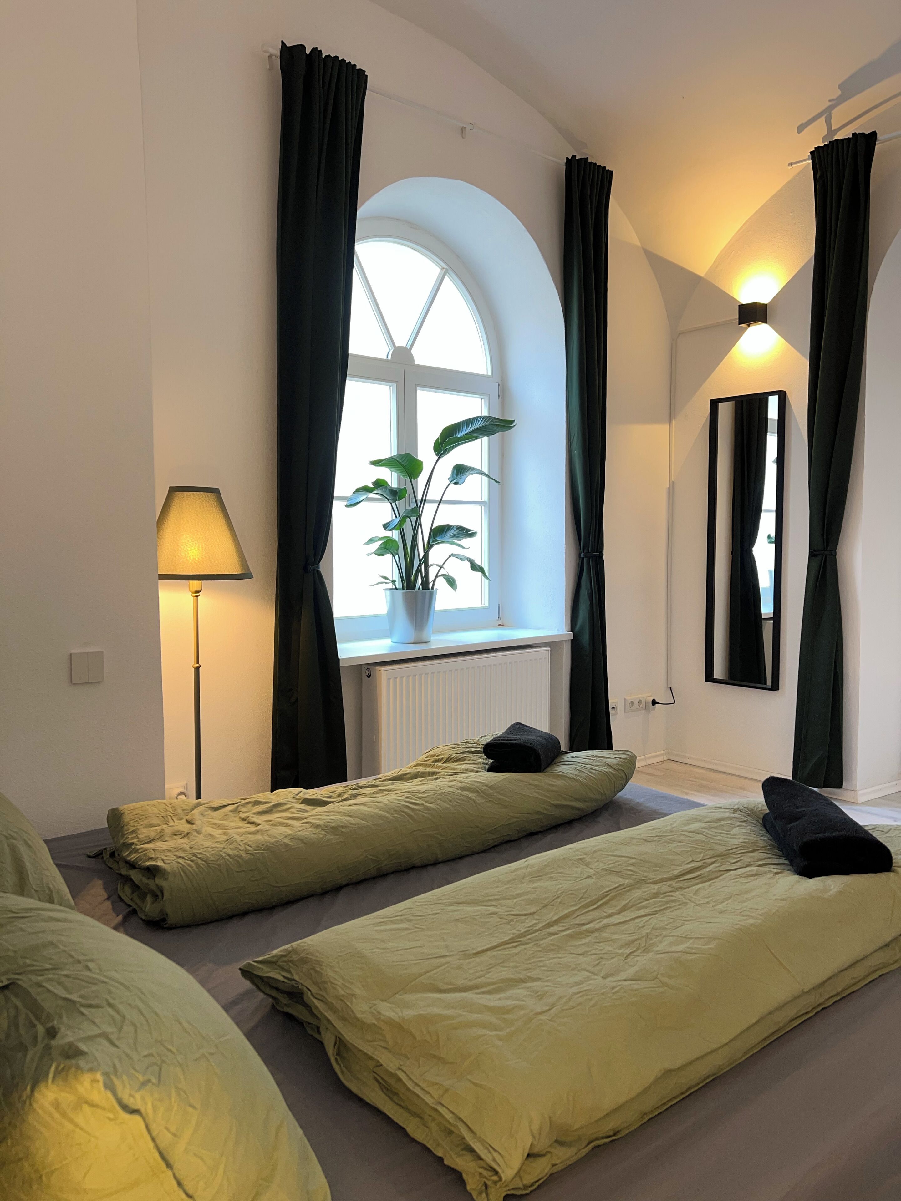 A room with two beds, a potted plant, a lamp, and a window with curtains.