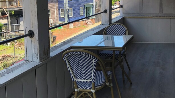 A covered patio with a table and two chairs, overlooking a blue house.