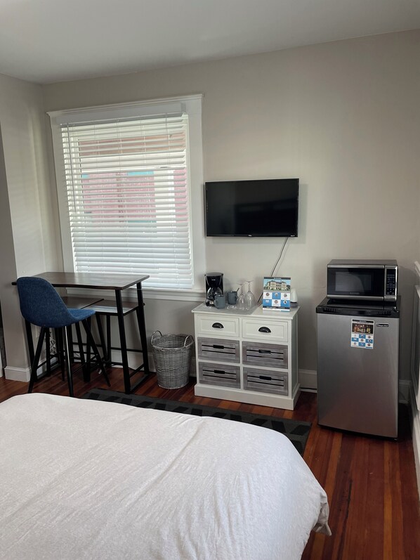 Una habitación de hotel con cama, escritorio con silla, televisión, microondas y refrigerador pequeño.