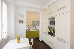 A modern kitchen with white cabinets, a dining table, and a vase with flowers. - Tasso Apartment (Rome)