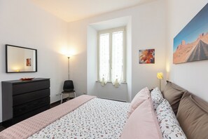 Une chambre à coucher avec un lit, une commode, une chaise, une fenêtre avec des rideaux et un tableau accroché au mur.