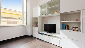 En moderne stue med et stort vindue, indbygget tv og hvide skabe.