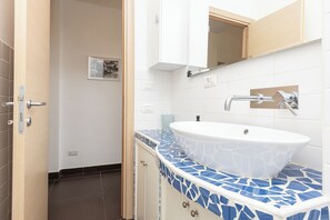 Une salle de bain avec un lavabo blanc, un plan de toilette en mosaïque bleue et une porte en bois.